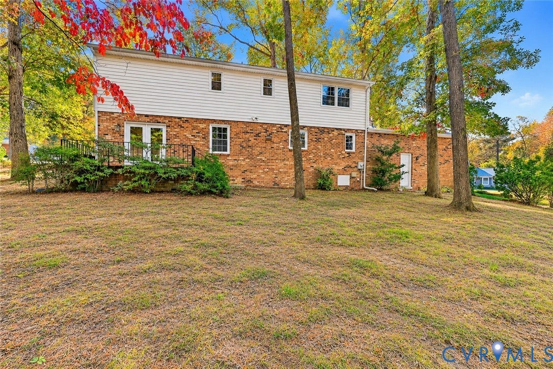 Two-story residence featuring a brick and white siding exterior, multi-pane windows, a raised metal railing deck, and mature trees on a lawn