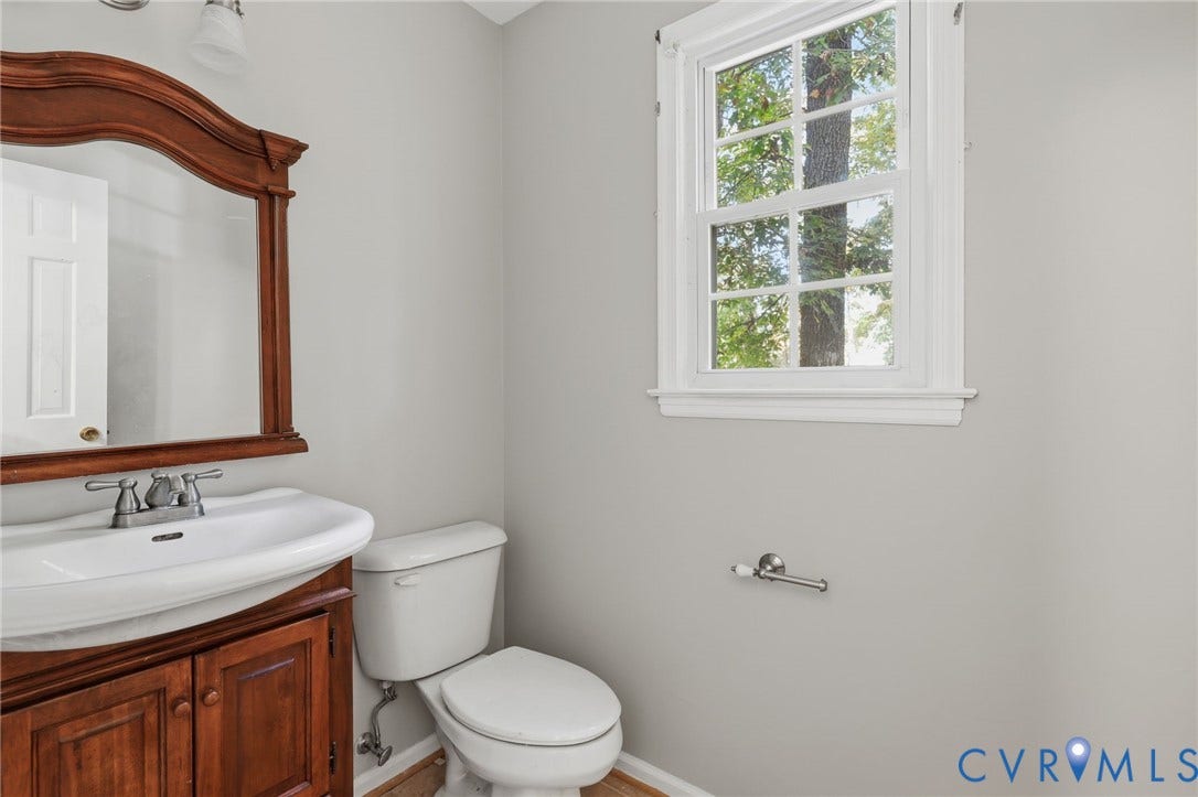 Bathroom featuring a wood-finish vanity with a drop-in sink, decorative arched mirror, double-hung window, and dual-handle chrome faucet