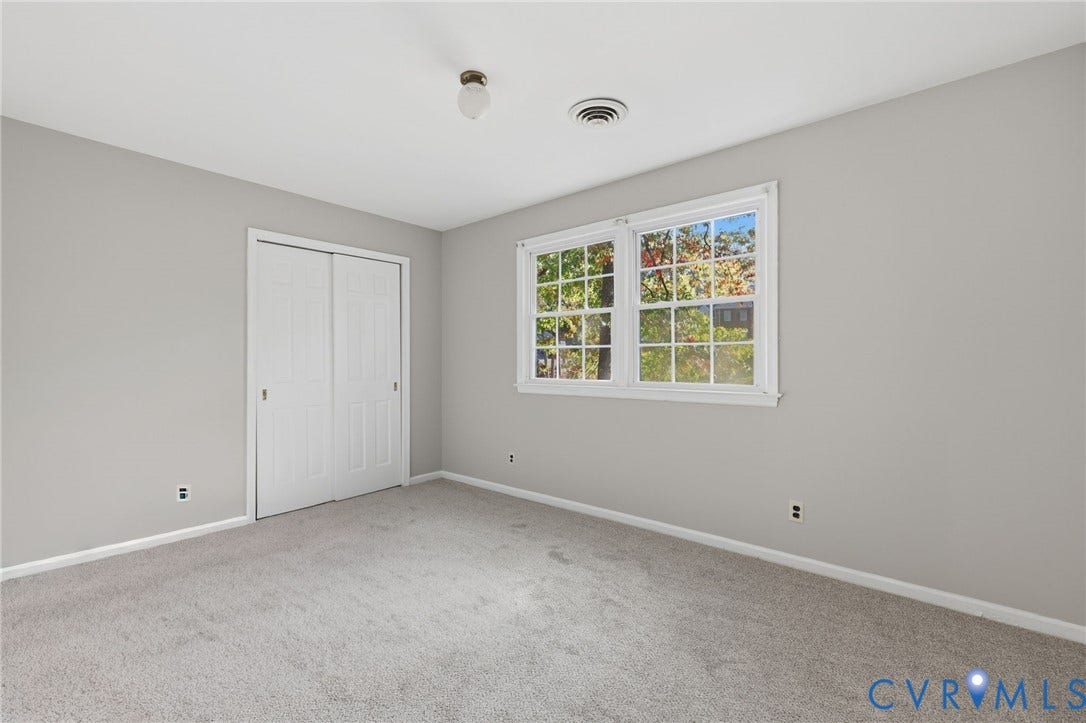 Neutral-toned room featuring wall-to-wall carpeting, dual-panel sliding closet doors, and a double-hung window with muntin grid detailing