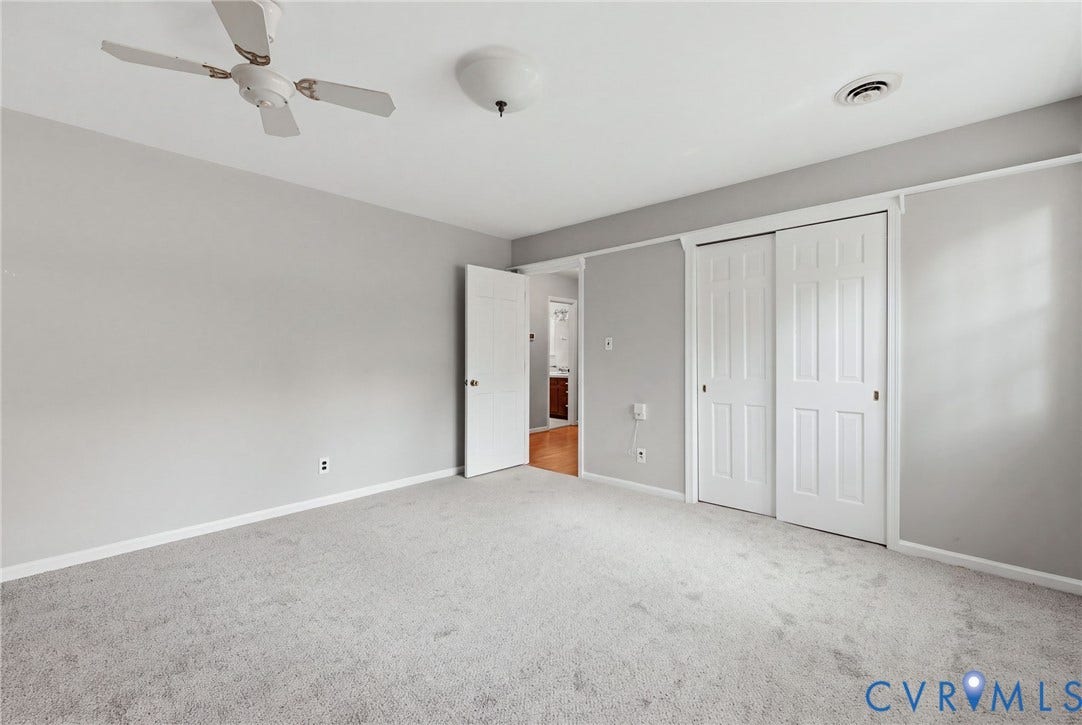 Neutral-toned interior featuring wall-to-wall carpeting, dual-panel sliding closet doors, and a ceiling fan with light fixture
