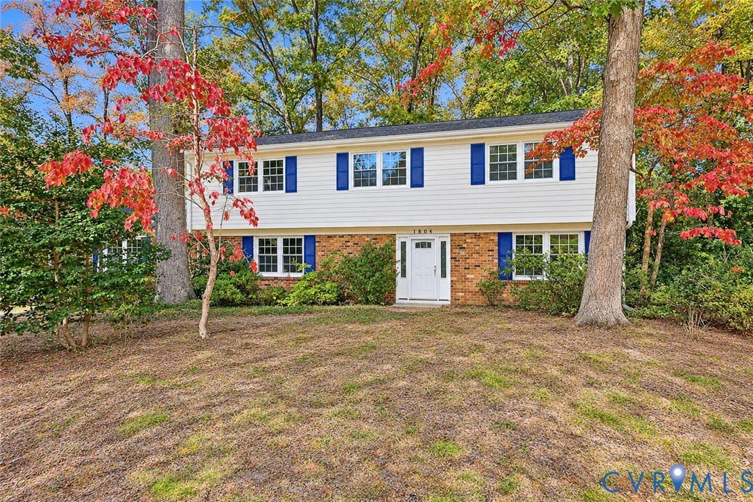 Two-story residence featuring light-colored horizontal siding, decorative blue shutters, and a brick veneer foundation