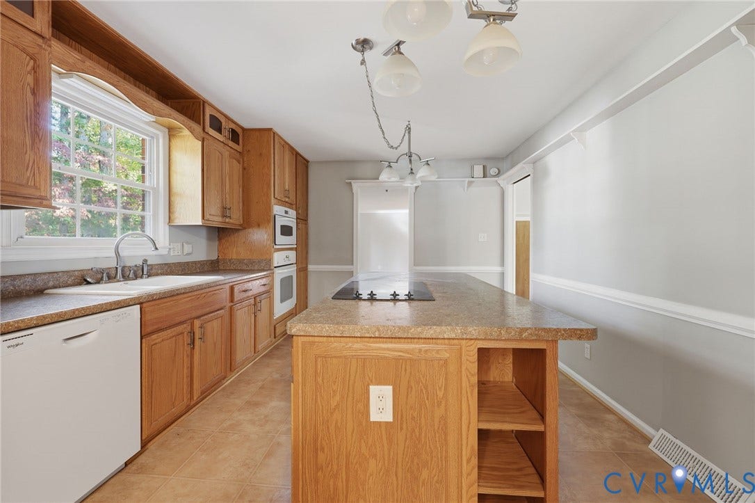 Kitchen featuring oak cabinetry, center island with integrated cooktop, stone-finish countertops, built-in wall oven, and tile flooring