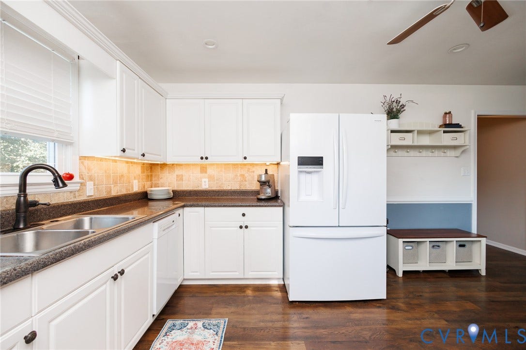 15525 Saddlebrook Road, Chesterfield, VA 23838 White cabinetry with dark hardware, stone-look countertops, tiled backsplash, stainless steel double basin sink with dark faucet, and wood-finish flooring