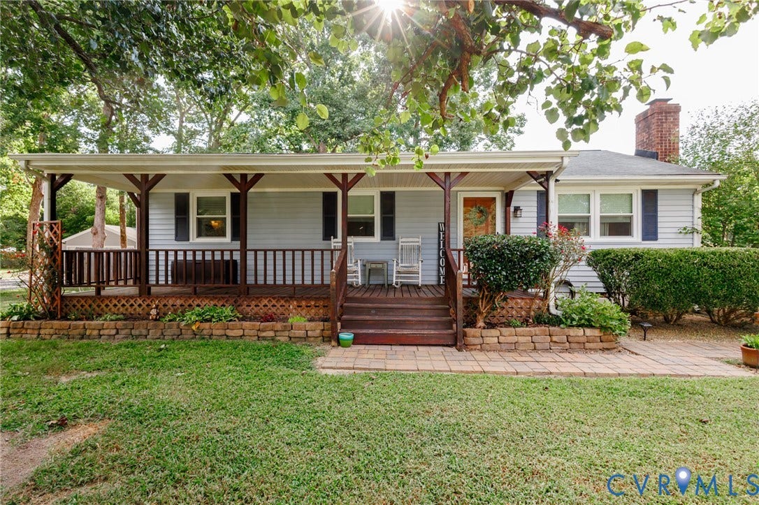 15525 Saddlebrook Road, Chesterfield, VA 23838 Light blue siding exterior with dark blue shutters, covered front porch with dark wood-finish railing and columns, brick chimney, and a stone retaining wall