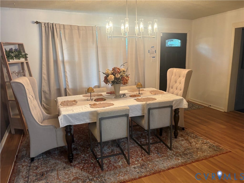 2443 Tignor Road, Richmond, VA 23224 Dining area featuring wood flooring, a window with draperies, a central chandelier, and a dark-paneled door with an arched glass insert