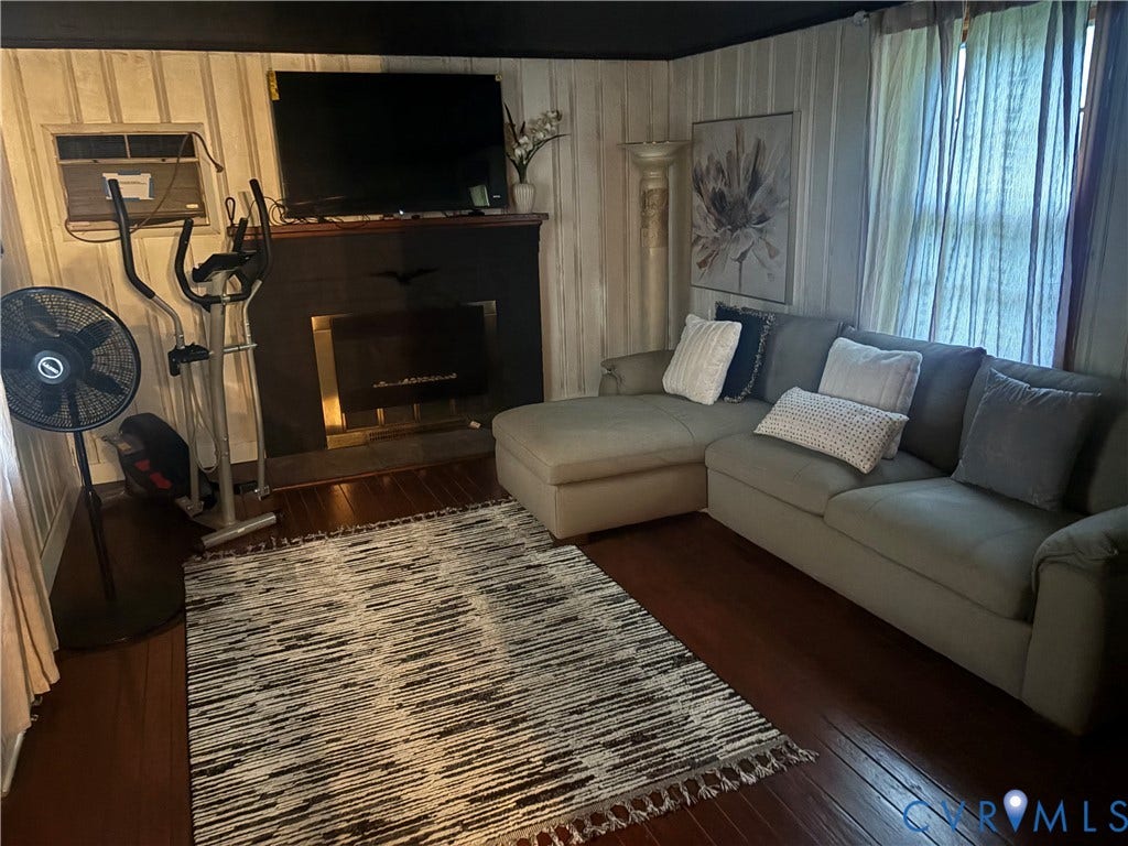 2443 Tignor Road, Richmond, VA 23224 Dark wood-finish flooring, accent wall paneling, and a fireplace with a dark mantel