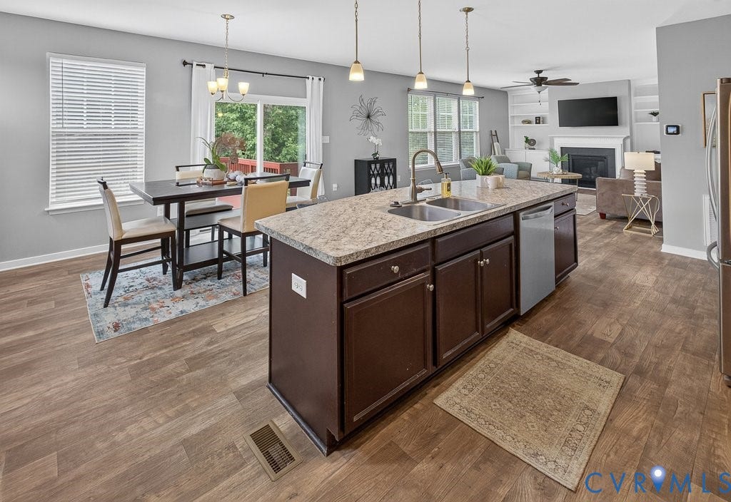 7401 Nicklaus Circle, Moseley, VA 23120 Open-concept living area featuring wood-finish flooring, a kitchen island with dual sinks and stone-finish countertop, dark wood cabinetry, and recessed lighting