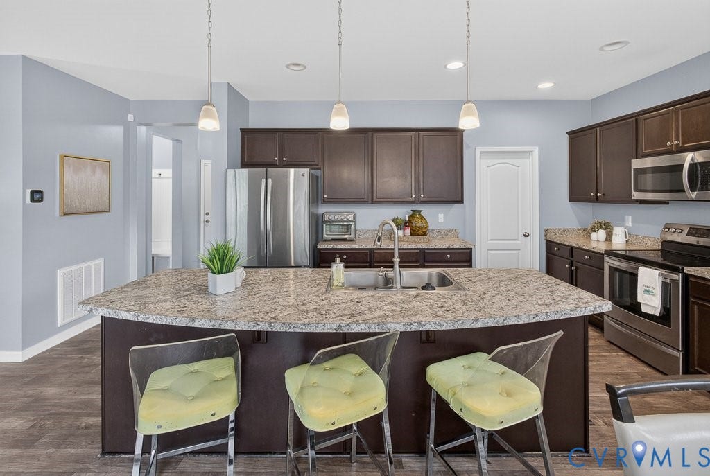 7401 Nicklaus Circle, Moseley, VA 23120 Kitchen featuring a large island with an undermount sink, pendant lighting, dark wood-finish cabinetry, and stainless steel appliances
