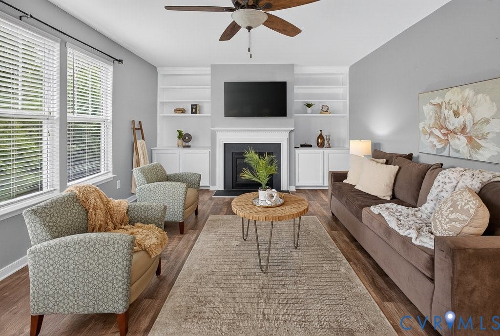 7401 Nicklaus Circle, Moseley, VA 23120 Living area featuring wood-finish flooring, a ceiling fan, multiple windows with blinds, built-in shelving, and a fireplace with a mantel