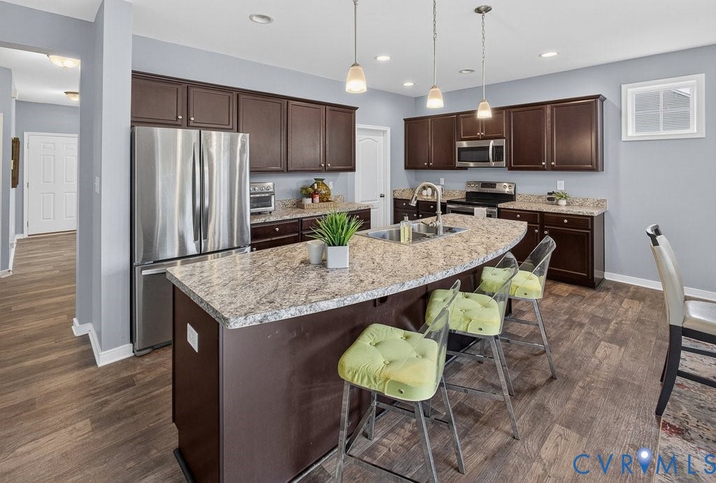 7401 Nicklaus Circle, Moseley, VA 23120 Kitchen featuring LVP, dark wood cabinetry, stainless steel appliances, and a central island with a sink and pendant lighting.