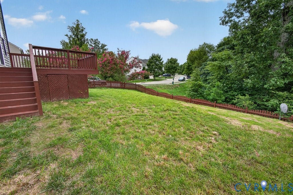 7401 Nicklaus Circle, Moseley, VA 23120 Newly seeded. Expansive yard featuring a wooden deck with railing, stairs, and lattice skirting, bordered by a low wooden fence and mature trees