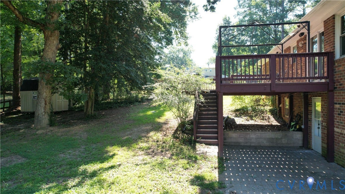 9018 Brucewood Drive, Midlothian, VA 23235 Elevated wood deck with railings, exterior brick wall, paved patio area, and mature trees