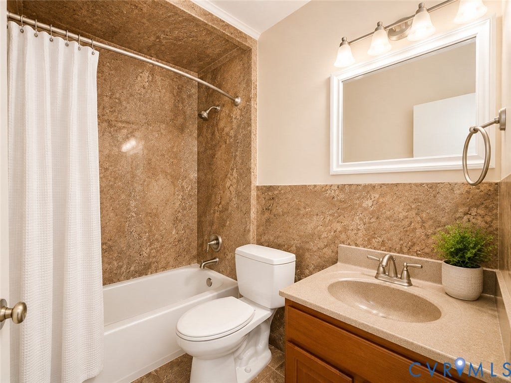 9018 Brucewood Drive, Midlothian, VA 23235 Bathroom featuring a built-in tub with a shower fixture, wall-mounted vanity light, framed mirror, and a wood-finish vanity with an integrated sink