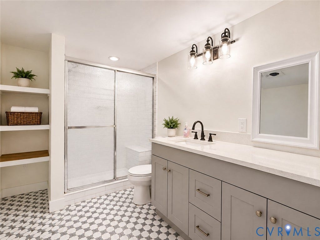 9018 Brucewood Drive, Midlothian, VA 23235 Spa-inspired primary bathroom featuring a frameless glass-enclosed shower with subway tile surround, dual-sink vanity with soft-close cabinetry and brushed nickel hardware, quartz countertop, black framed mirror, and geometric tile flooring