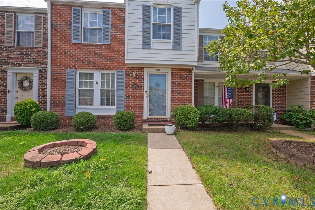 Brick exterior, light gray window shutters, white-framed windows, concrete walkway, brick-lined fire pit