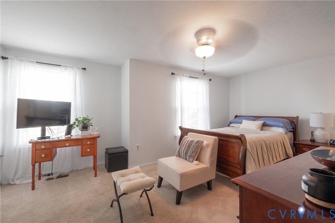 Carpeted flooring, two windows with curtain rods, and a ceiling fan with integrated lighting