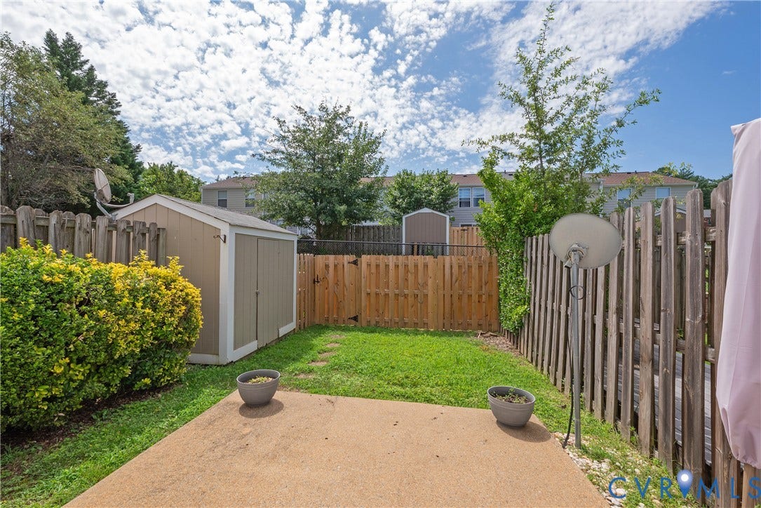 Private backyard featuring a concrete patio, green lawn, wood fence, and storage shed