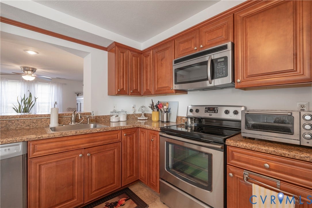 Wood-finish cabinetry, stainless steel appliances, speckled countertops, and a stainless steel sink with a mounted faucet
