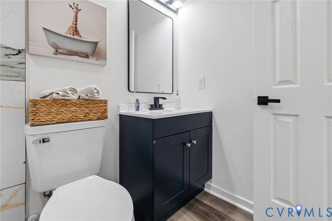 516 S South Street, Myers, Petersburg, VA 23803 White panel door with matte black hardware, dark blue vanity with silver hardware, rectangular mirror, white countertop, and wood-finish flooring
