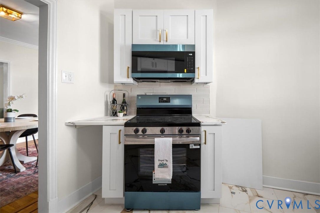 3510 Hanover Avenue, Museum District, Richmond, VA 23221 White shaker-style cabinetry with gold-tone hardware, a stainless steel and blue range, an over-the-range microwave, and light-toned countertops