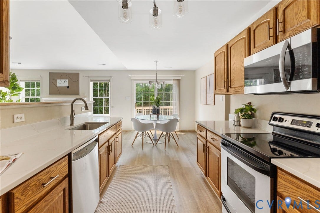 3173 Poplar View Place, Ashley Forest, Chester, VA 23831 Open-concept kitchen featuring wood cabinetry, light countertops, and stainless steel appliances, with wood-finish flooring extending to the dining area with a glass sliding door