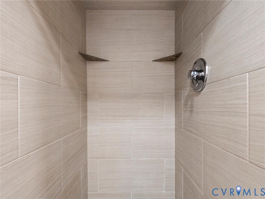 Tiled shower enclosure featuring light-toned large format tiles, a chrome shower control, and built-in corner shelves