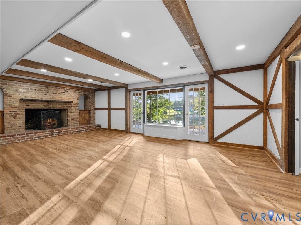 Exposed wood beams, wood-finish flooring, brick fireplace, recessed lighting, and French doors leading to exterior