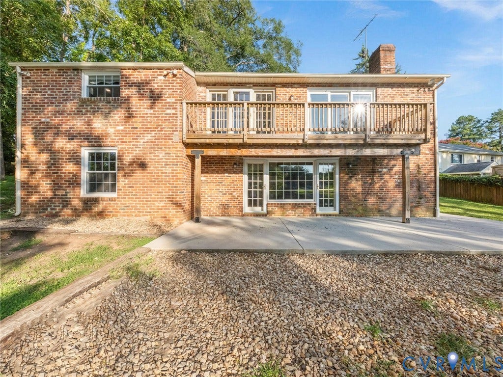 Brick exterior featuring a wood balcony, ground-level patio, multiple windows, and a glass-paneled door