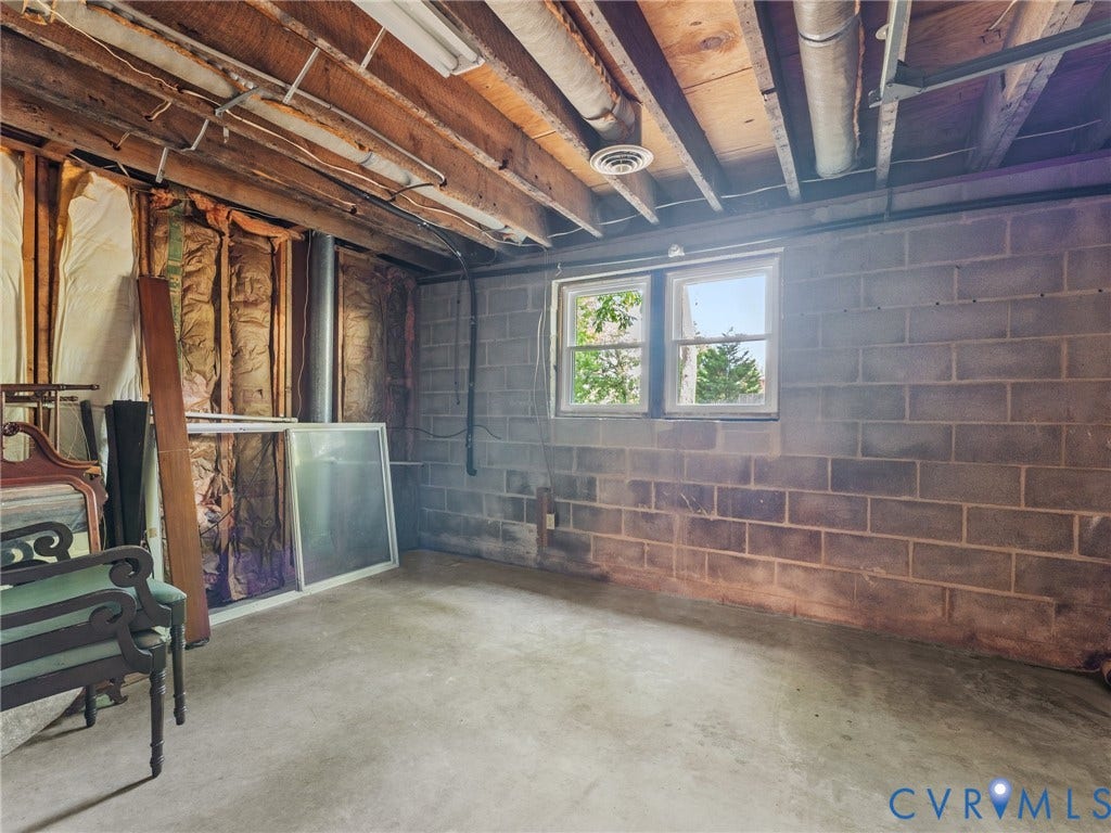 Unfinished basement space with exposed brick walls, concrete flooring, and open ceiling with mechanical systems