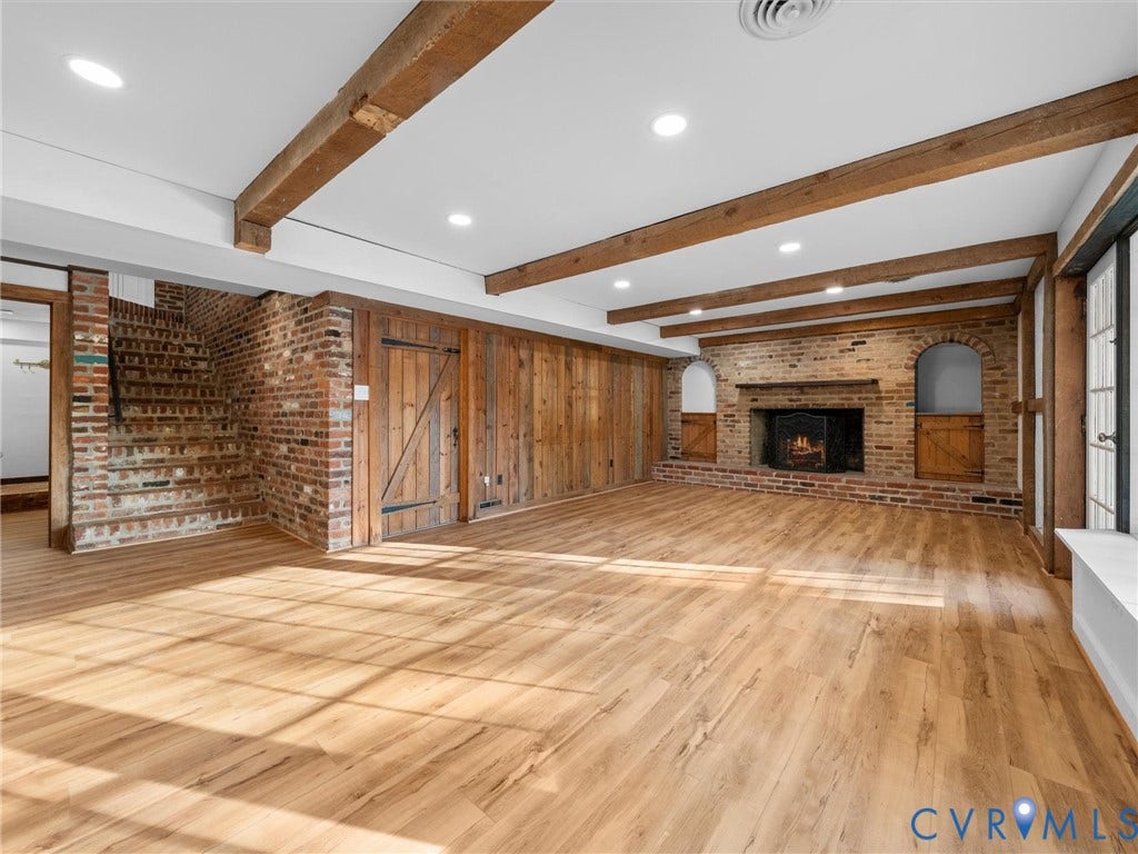 Exposed wood beams, wood-finish flooring, brick accent walls, built-in fireplace, and recessed lighting