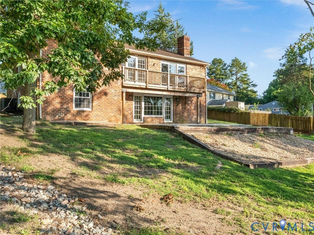 Brick exterior featuring a wood balcony, ground-level patio, and a tiered landscaped area