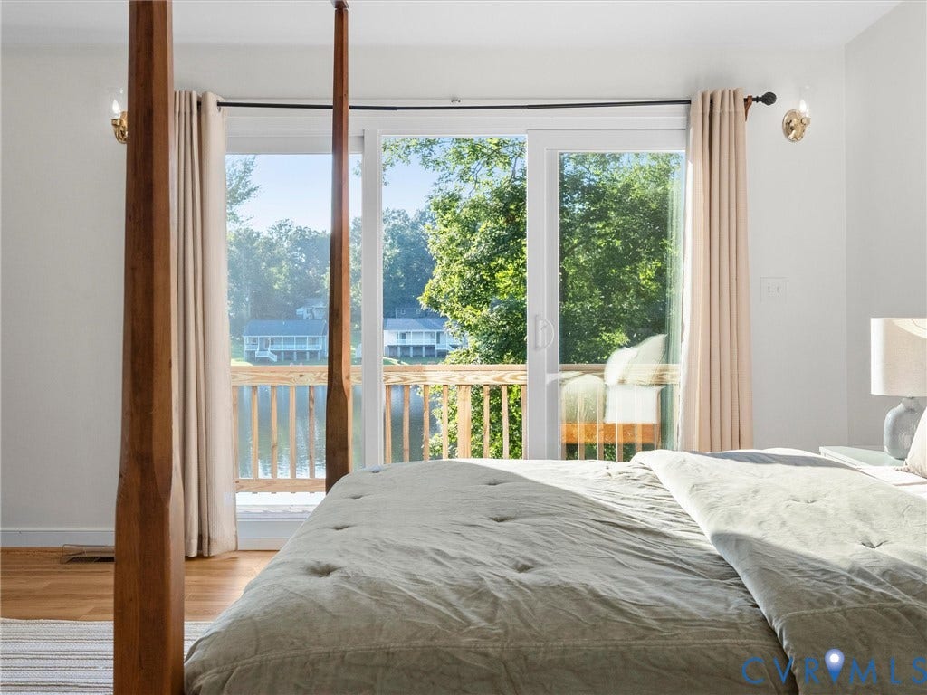 Sliding glass doors opening to a private balcony with natural wood railing, light wood-finish flooring, and wall-mounted sconces