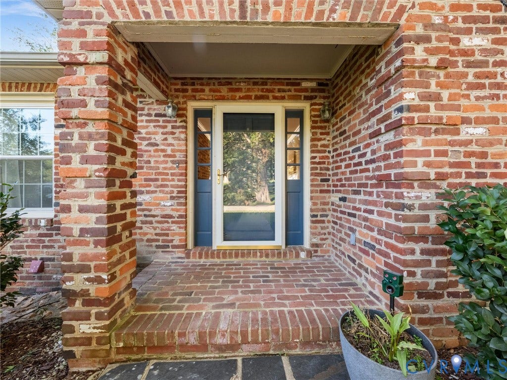 Brick exterior with a covered entry, featuring a brick-paved porch and a paneled entry door with sidelights