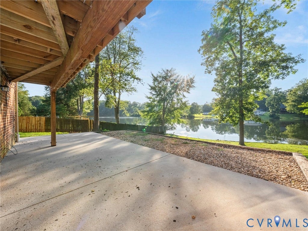 Under-deck patio with concrete surface, gravel landscaping, and a wooden privacy fence, overlooking a body of water