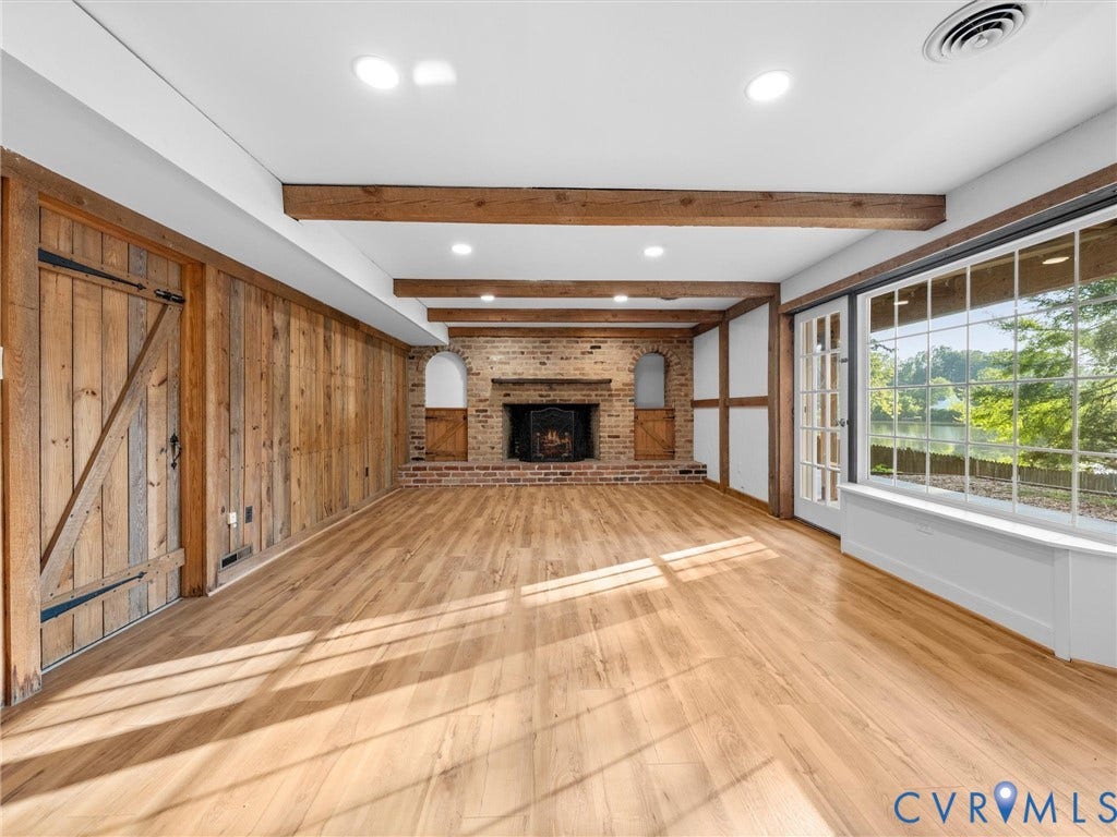 Exposed wood ceiling beams, brick-faced fireplace, wood-finish flooring, full-lite French doors, and a built-in window bench