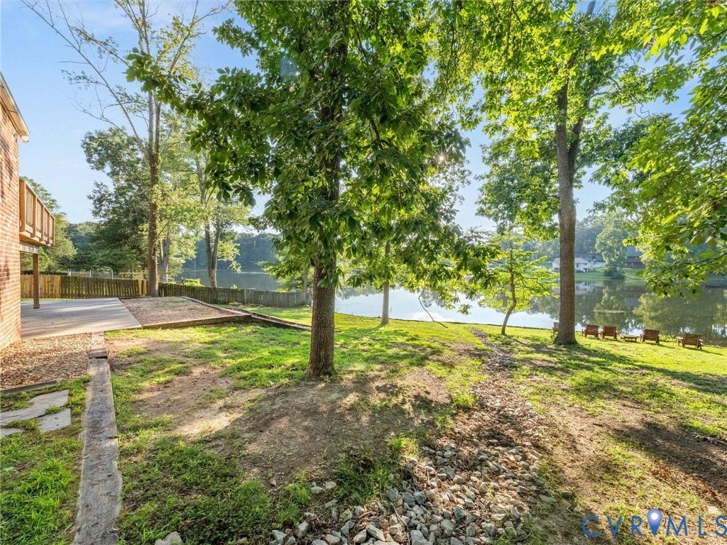 Waterfront property featuring a private deck, expansive yard, mature trees, and a wooden privacy fence