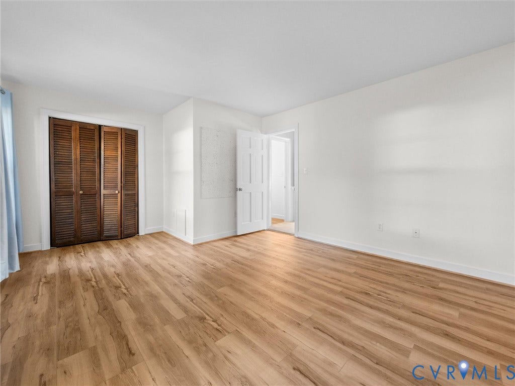 Light wood-finish flooring, white painted walls, louvered bi-fold closet doors, and white trim