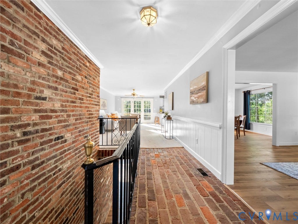 Exposed brick wall and flooring, white wainscoting, crown molding, and an iron balustrade with ornate detailing