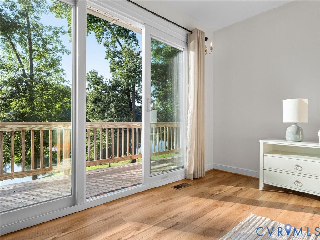 Sliding glass door opening to a private wooden deck, surrounded by mature trees and visible water