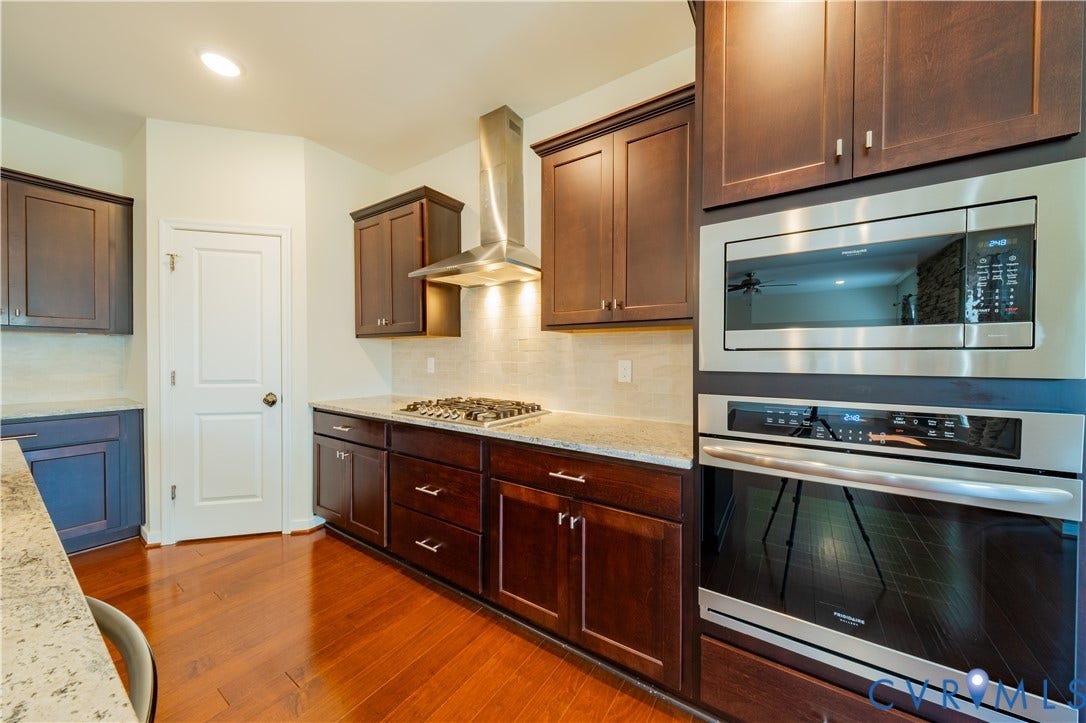 Kitchen featuring wood-finish flooring, dark wood cabinetry, light-toned countertops, stainless steel appliances, and a tiled backsplash