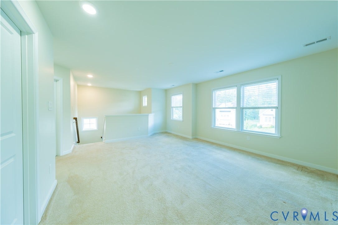 Carpeted room featuring multiple windows, recessed ceiling lighting, and a white balustrade