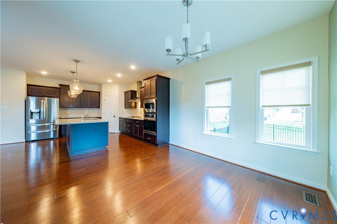 Expansive wood-finish flooring, recessed lighting, central kitchen island with pendant lighting, stainless steel appliances, and multiple windows with roller shades