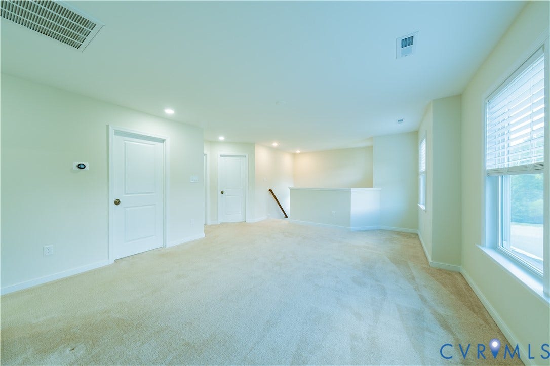 Spacious room with plush carpet flooring, recessed lighting, white paneled doors, and multiple windows with blinds