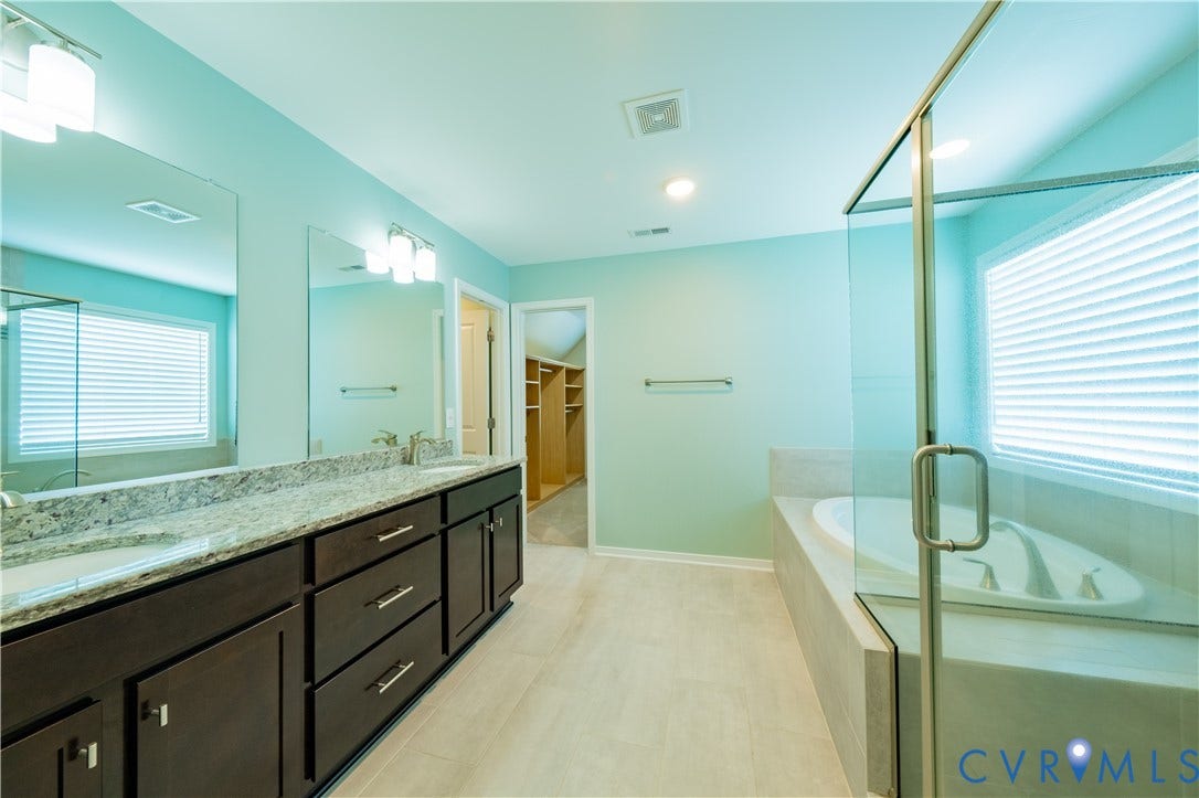 Dual vanity with stone countertop, separate shower enclosure with glass surround, built-in soaking tub, and organized walk-in closet
