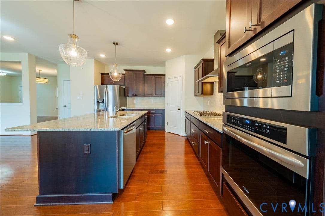 Kitchen featuring wood-finish flooring, stainless steel appliances, dark wood cabinetry, a center island with a light-toned countertop, and pendant lighting