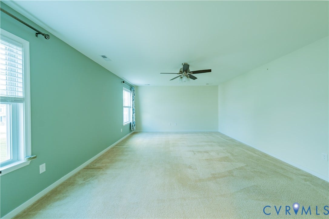 Expansive room featuring light-colored carpeting, multiple windows for natural light, a ceiling fan, and a neutral color palette