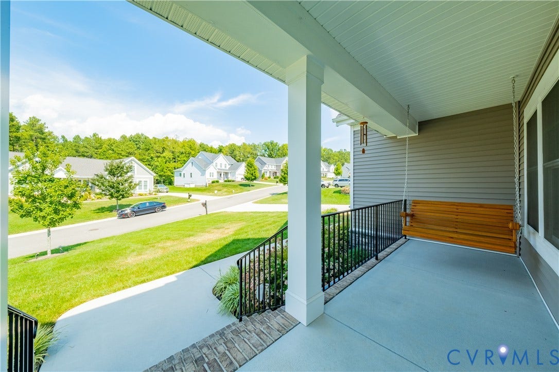 Inviting covered front porch with a wood-finish porch swing, white columns, black metal railings, and grey siding