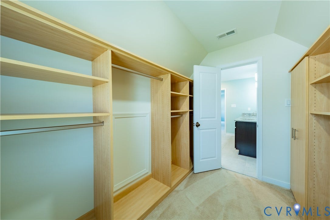 Built-in shelving and hanging rods, light-toned carpeting, white interior door, and an angled ceiling
