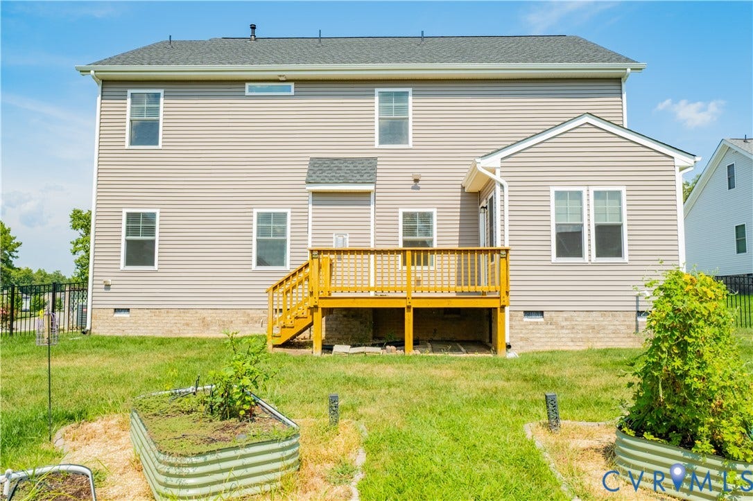 Two-story residential structure with light-colored siding, a wooden deck, and a brick foundation