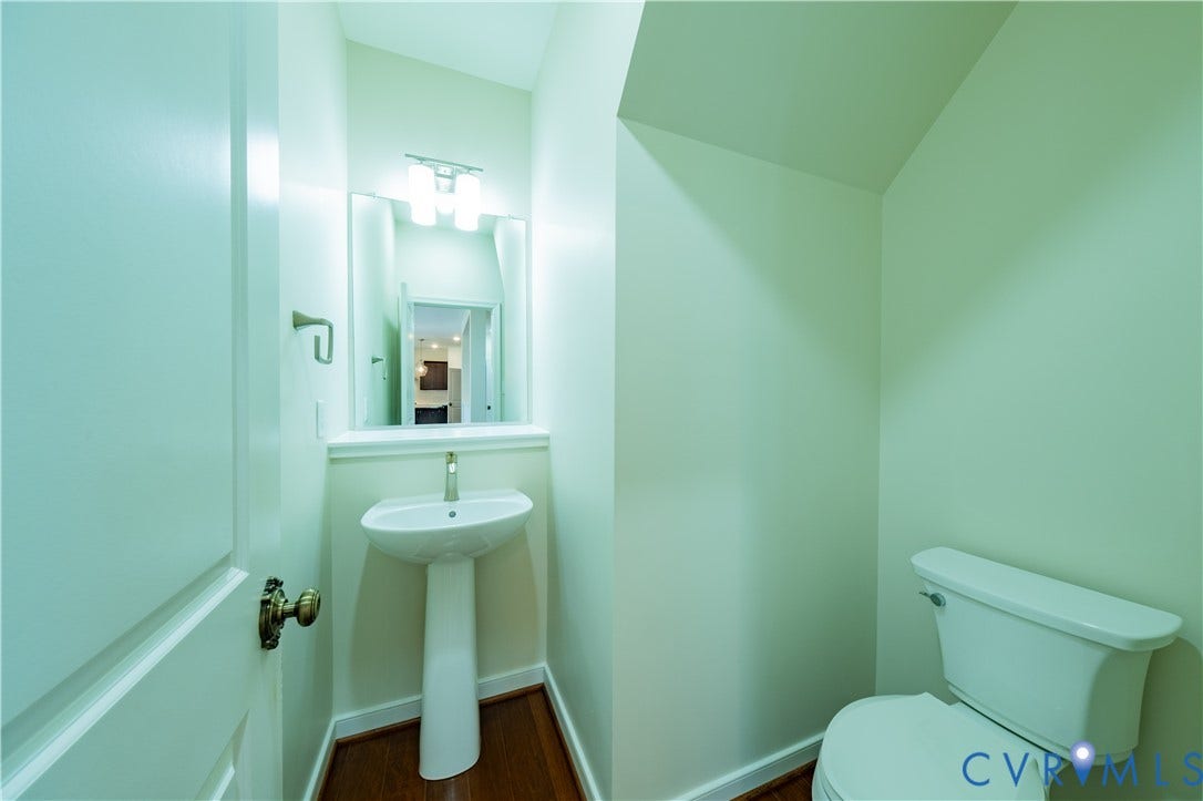 Pedestal sink with a wall-mounted faucet, vanity mirror with overhead lighting, and wood-finish flooring